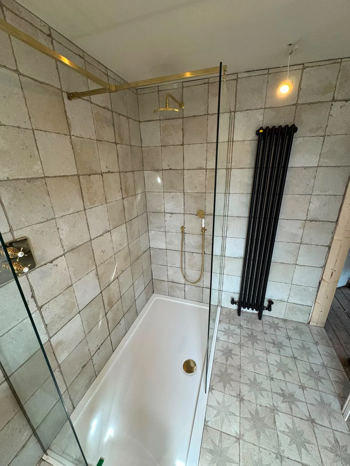 Walk-in shower installation with brass fittings and feature radiator by Infinite Plumbing & Heating