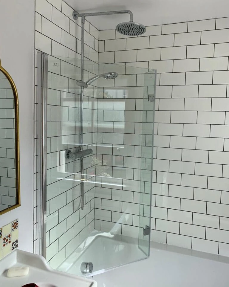 Modern shower enclosure with transparent glass, wall-mounted showerhead, and white tiled walls. Bright and elegant bathroom design.