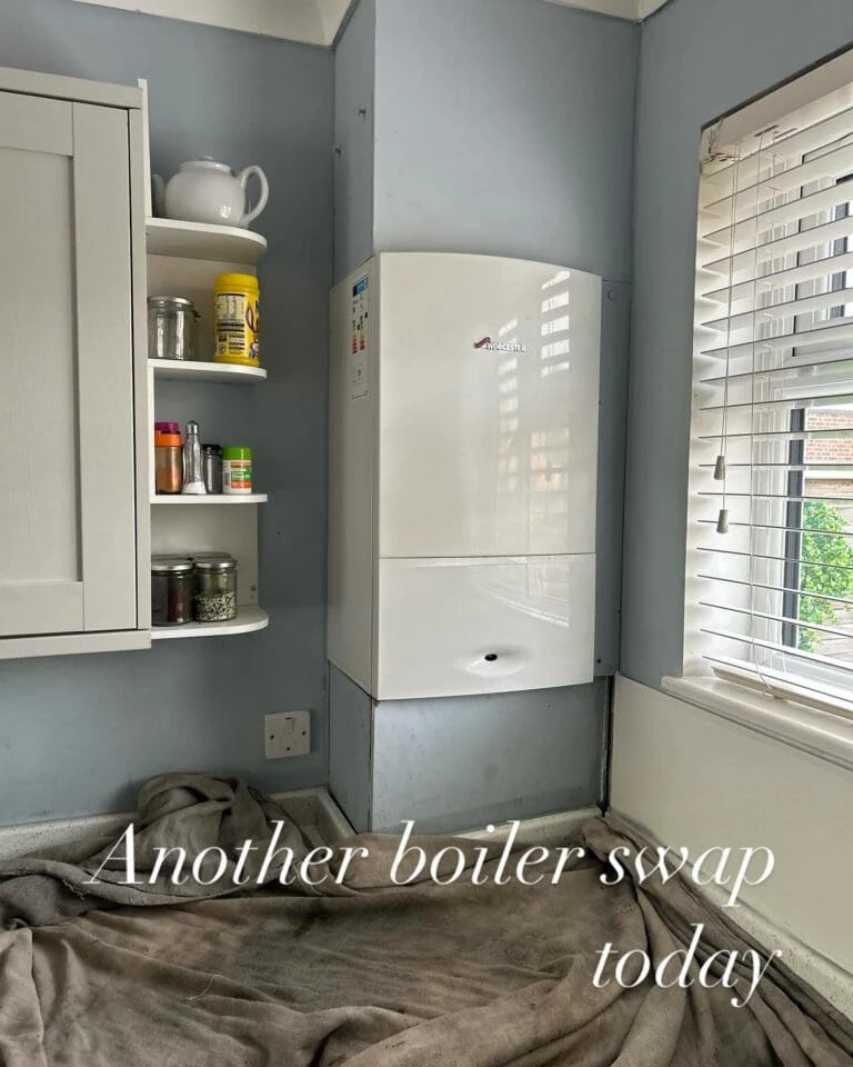 A clean kitchen corner featuring a new white boiler, shelves with jars and spices, and sunlight filtering through a window.