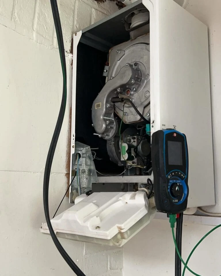 A partially open boiler panel revealing internal components and a digital testing device nearby.