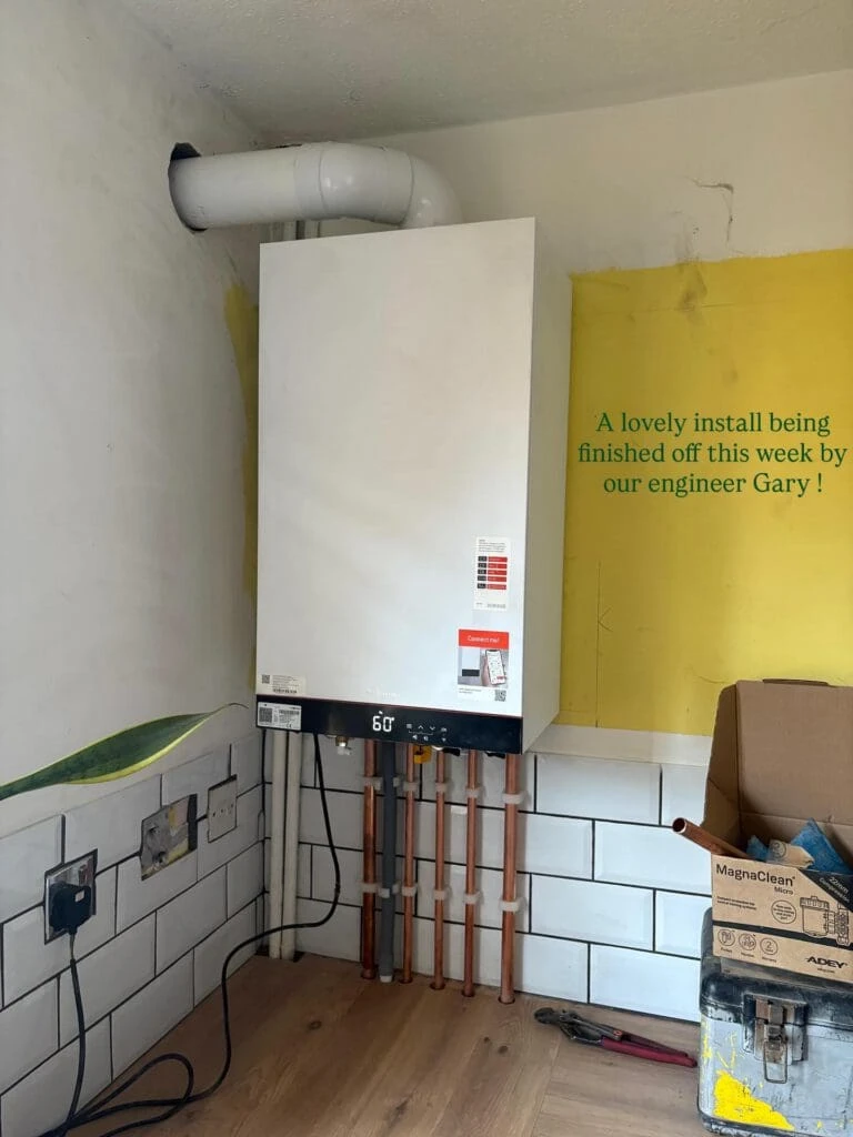 Newly installed boiler with pipes, electrical outlets, and a yellow wall sign about the installation by engineer Gary.