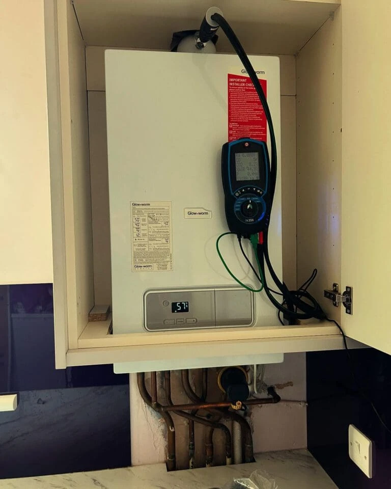 Boiler installed in a kitchen cabinet, displaying its control panel and temperature reading, alongside visible plumbing connections.