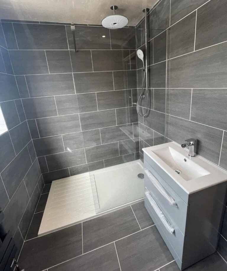 Modern bathroom featuring a walk-in shower with gray tiles, a glass partition, and a gray vanity with a sink.