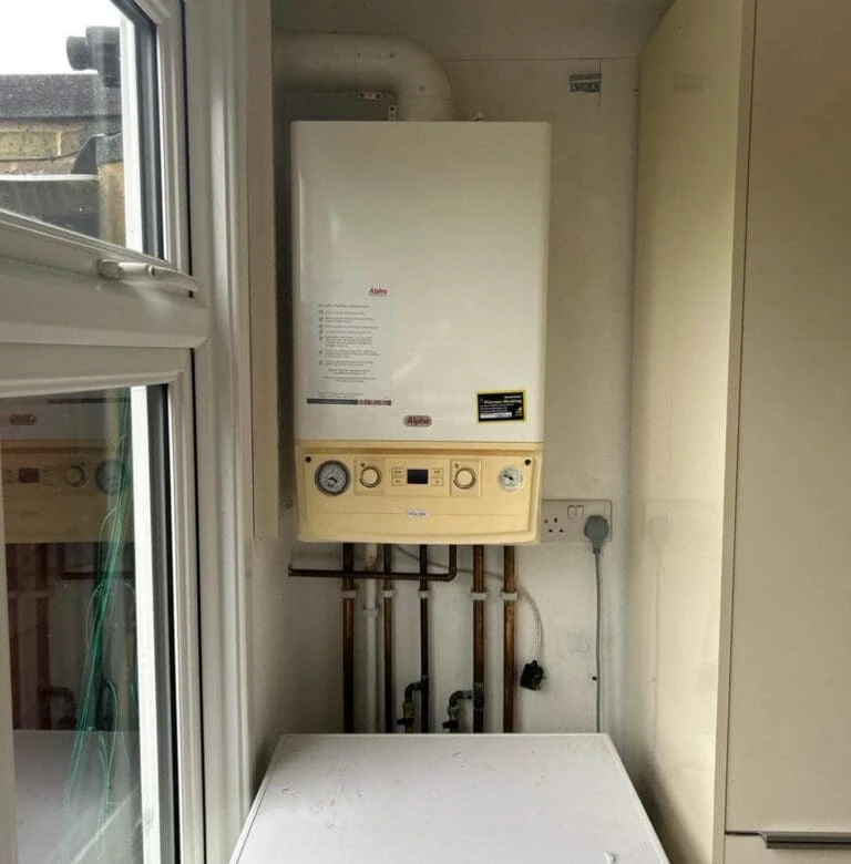 A white boiler mounted on the wall with control panel and gauges, surrounded by pipes, in a well-lit utility space.