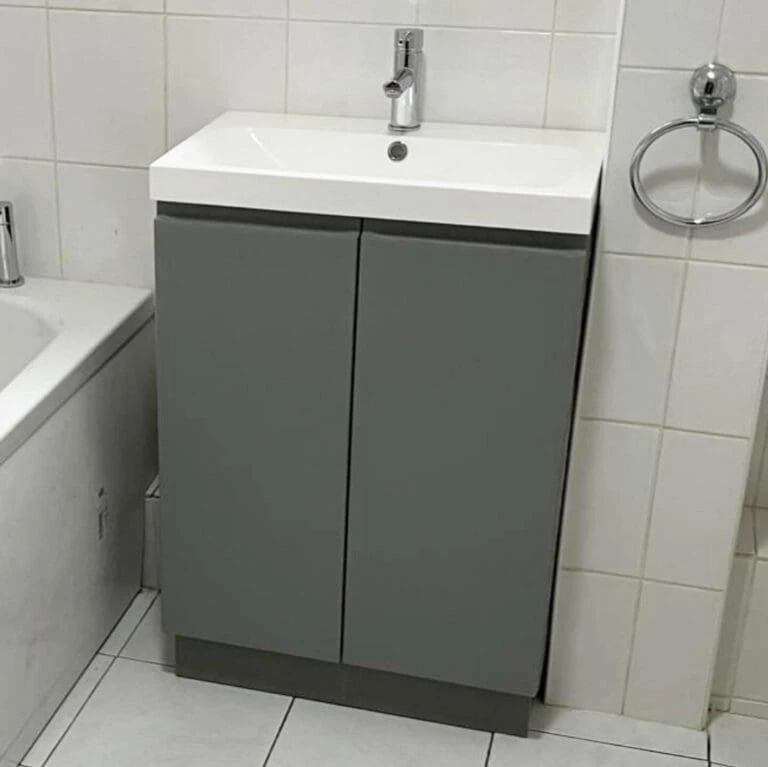 Modern bathroom sink cabinet with a white countertop and gray doors, adjacent to a bathtub and tiled wall.