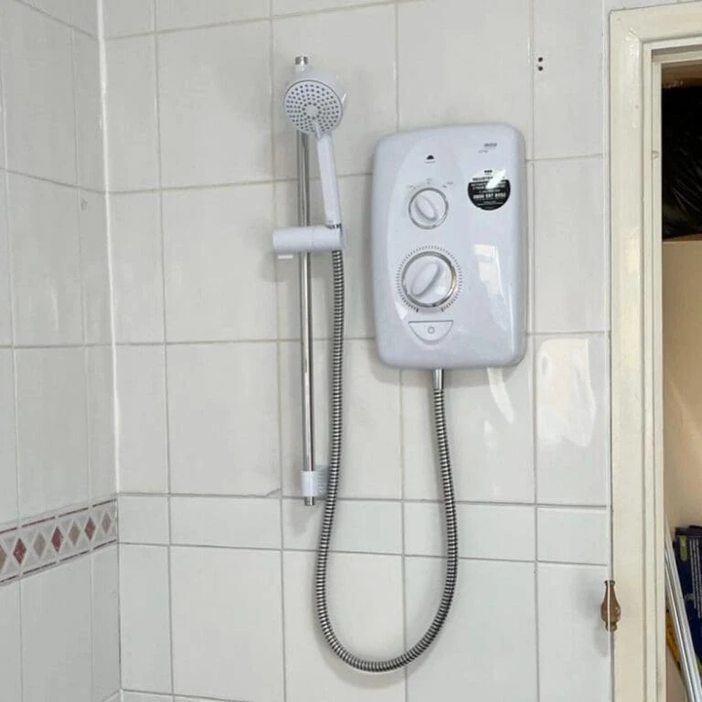A wall-mounted shower unit with a handheld showerhead is installed against tiled walls, next to an open door.